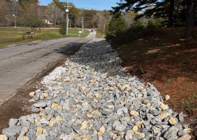 Stone-lined drainage ditch installation to prevent erosion on a graded slope